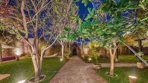 A stone pathway leading through a garden with trees and illuminated planters. - Hôtel Riad Caravan Serai (Marrakech)