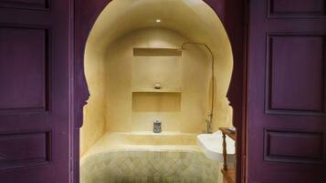 A bathroom with a tiled floor, a sink, a mirror, and a shelf with a small decorative item.