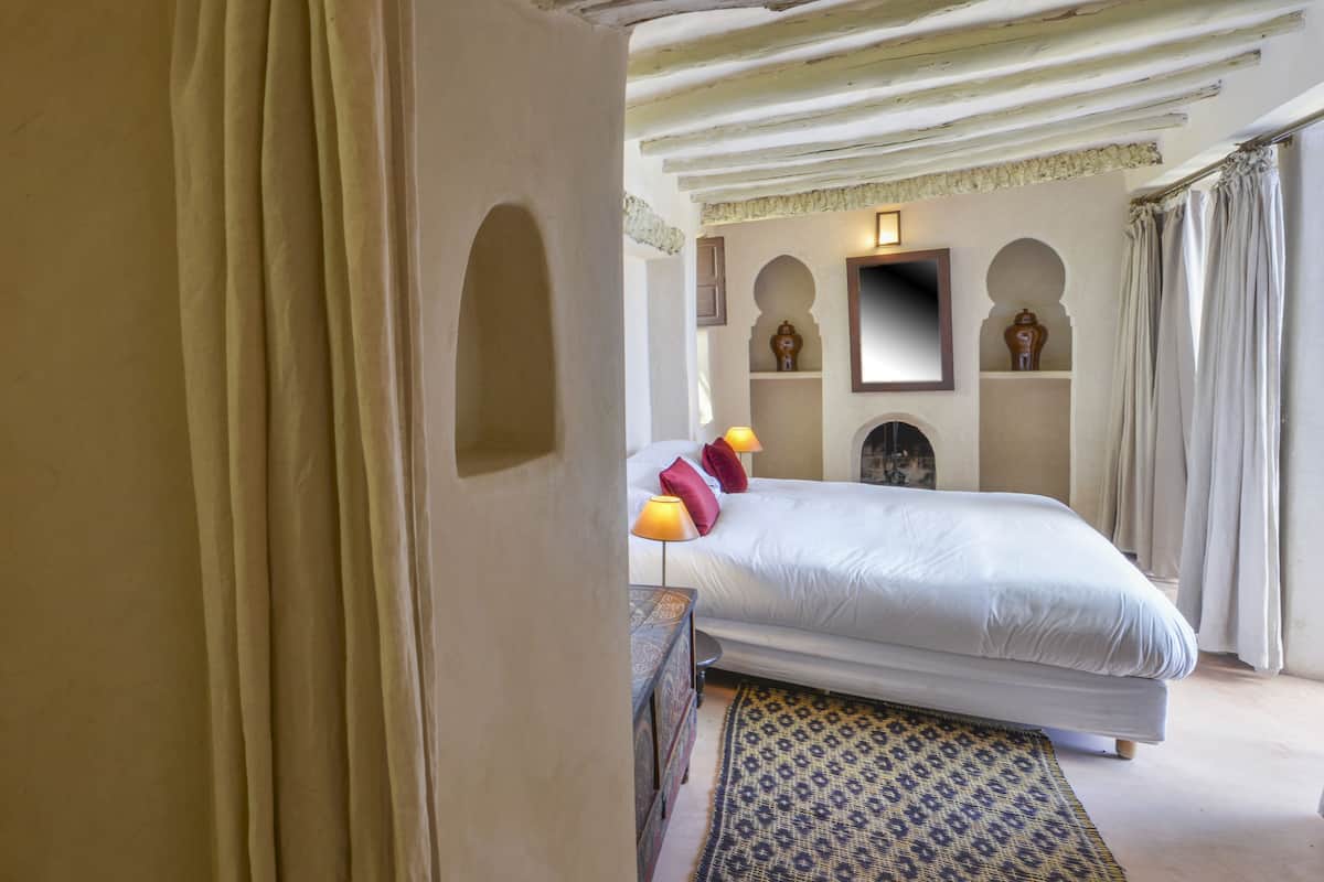 A bedroom with a large bed, a nightstand, a patterned rug, and decorative wall sconces.