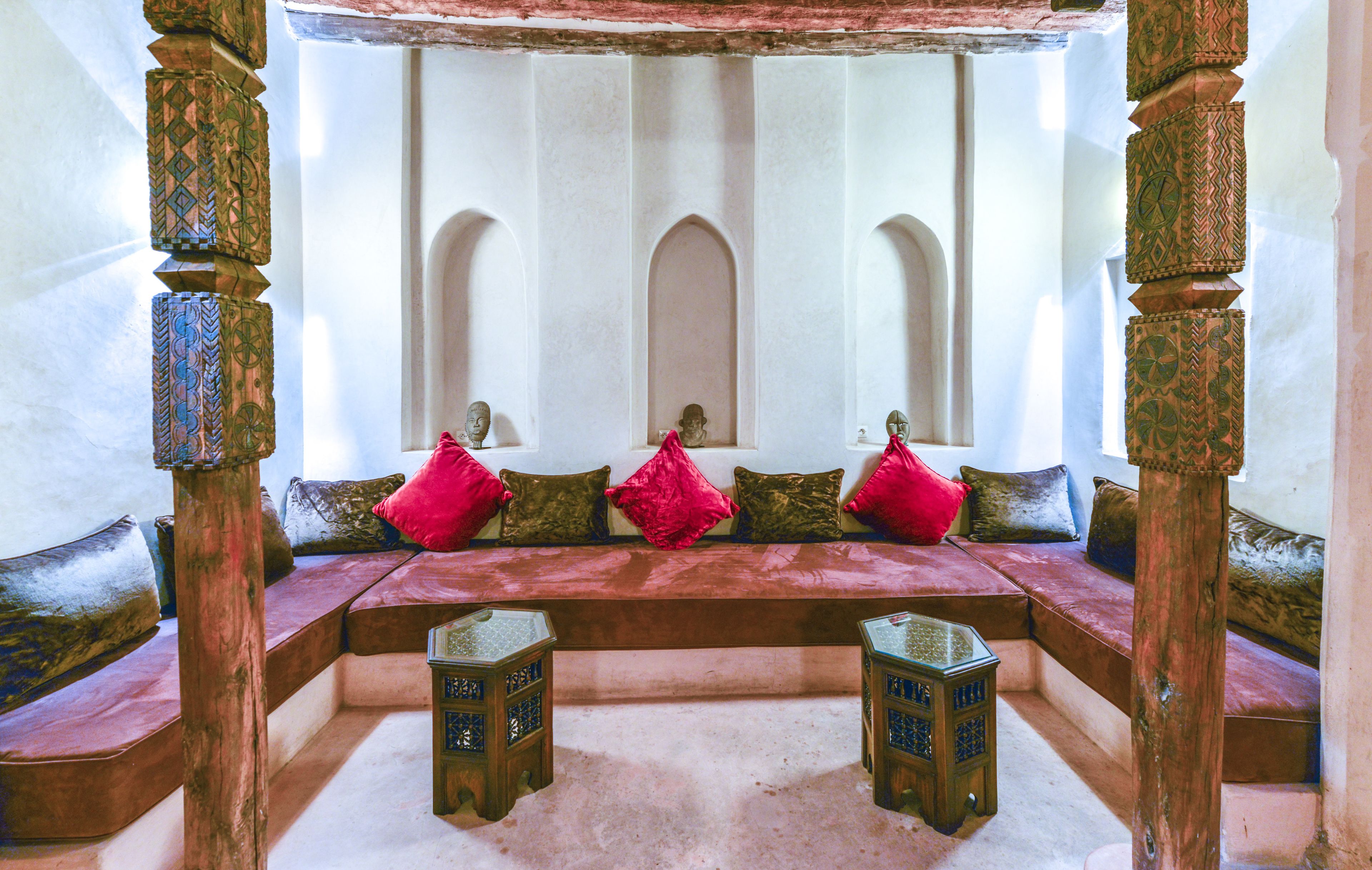 A traditional room with a bench, cushions, and ornate wooden columns.