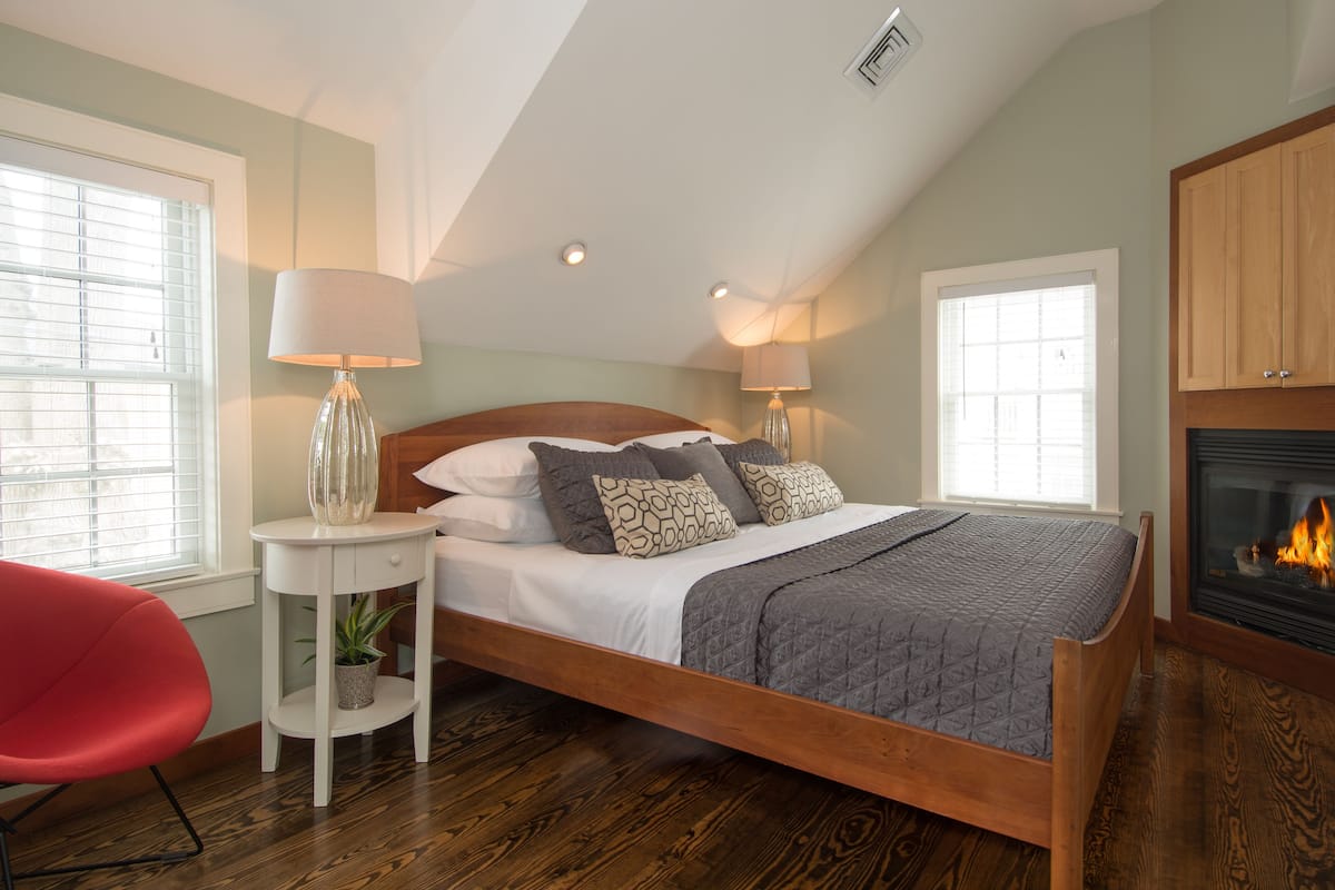 A bedroom with a wooden bed, two bedside lamps, a red chair, and a fireplace.