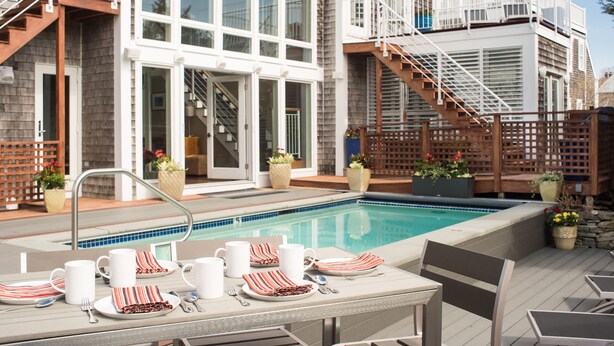 A poolside area with a dining setup, a staircase, and a view of a building with large windows and a balcony. - 8 Dyer Hotel (Provincetown)