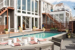 Ein Poolbereich mit Essbereich, einer Treppe und Blick auf ein Gebäude mit großen Fenstern und einem Balkon.