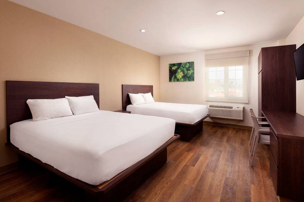 A hotel room with two beds, a TV, a window, and a painting on the wall.