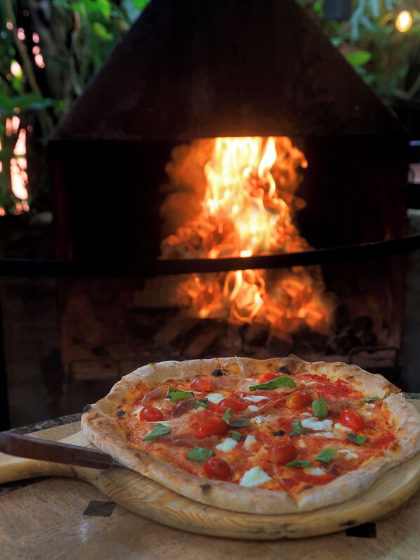 Una pizza frente a un horno de leña.