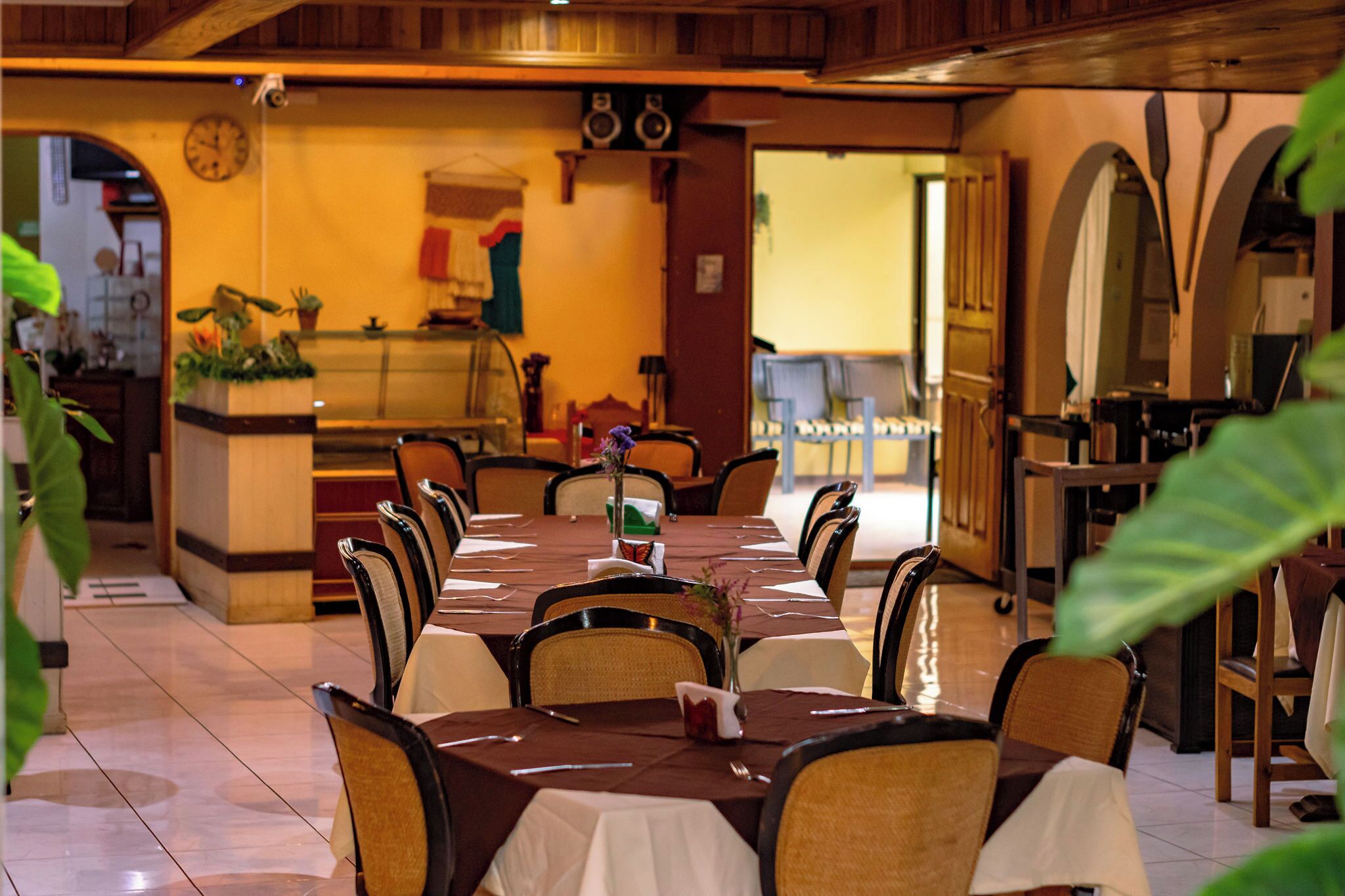 A restaurant with a long dining table, chairs, and a counter area with a clock and decorative items.