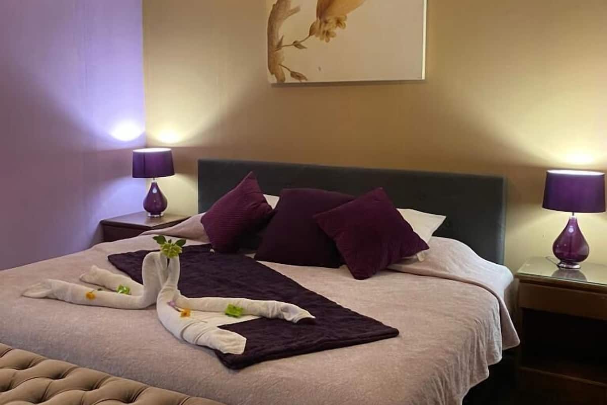 A hotel room with a large bed, two nightstands, a bench, and a wall-mounted artwork.