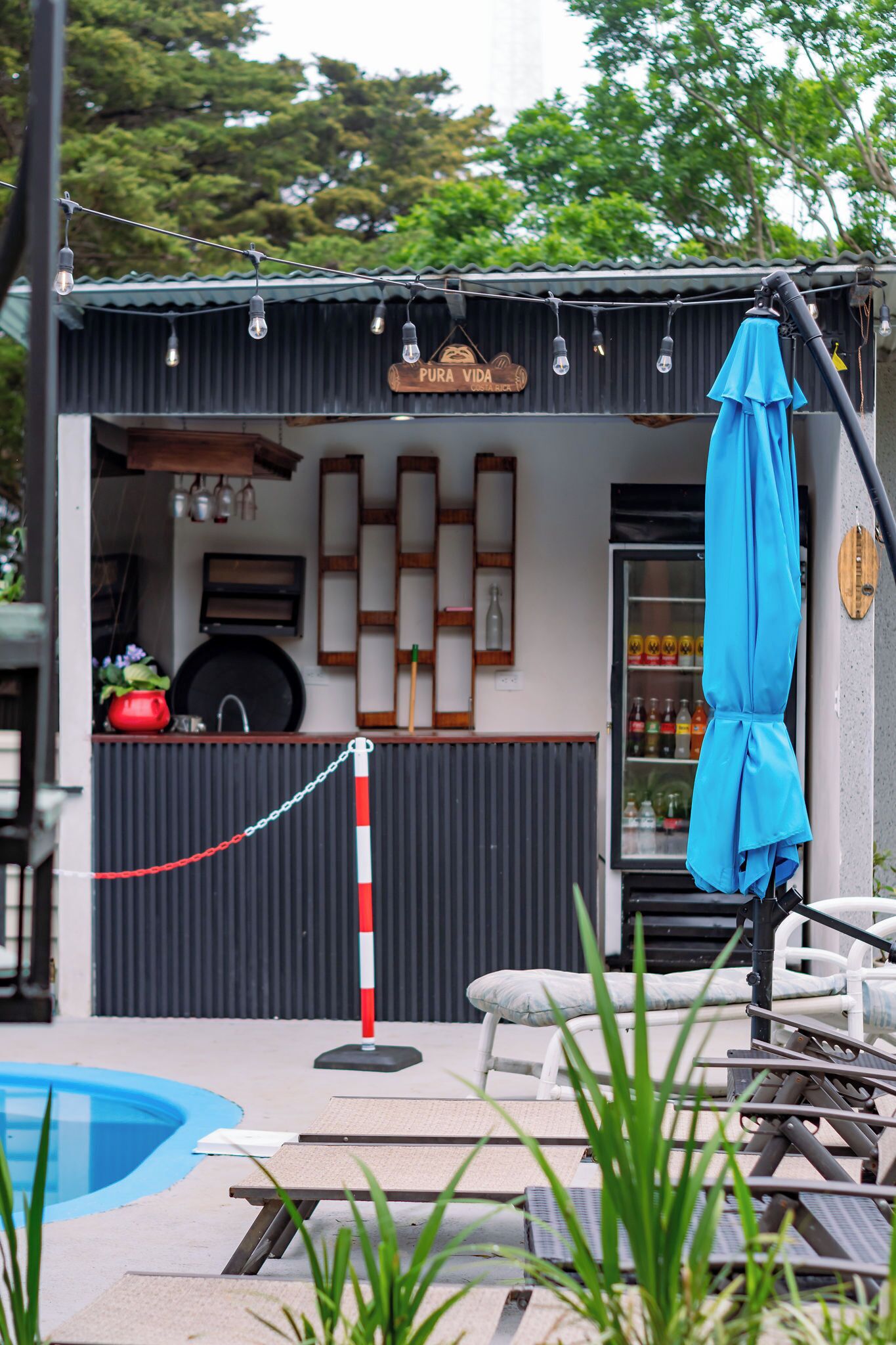 A small outdoor seating area with a pool, a blue umbrella, and a refrigerator stocked with beverages.