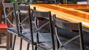 A restaurant interior with wooden tables and black chairs, a chalkboard menu, and string lights.