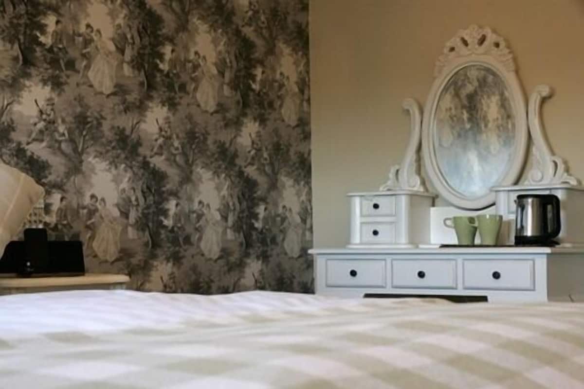 A bedroom with a bed, a dresser with a mirror, and a floral wallpaper.