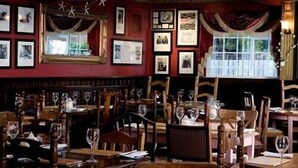 A restaurant interior with wooden tables and chairs, framed pictures on the walls, and a window with curtains. - The Lambton Worm (Chester-le-Street)