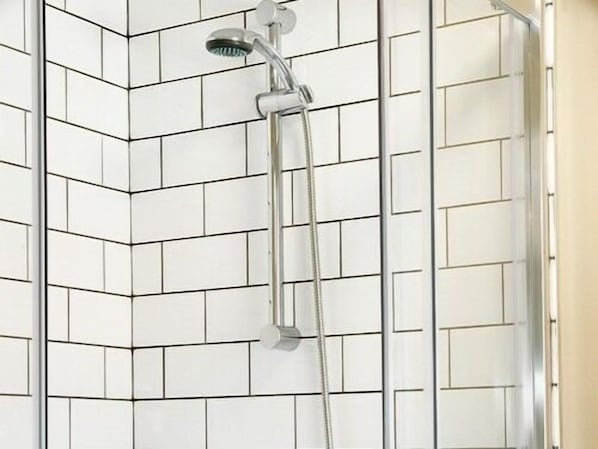 Canto de um banheiro com paredes revestidas de azulejos brancos e área de chuveiro.