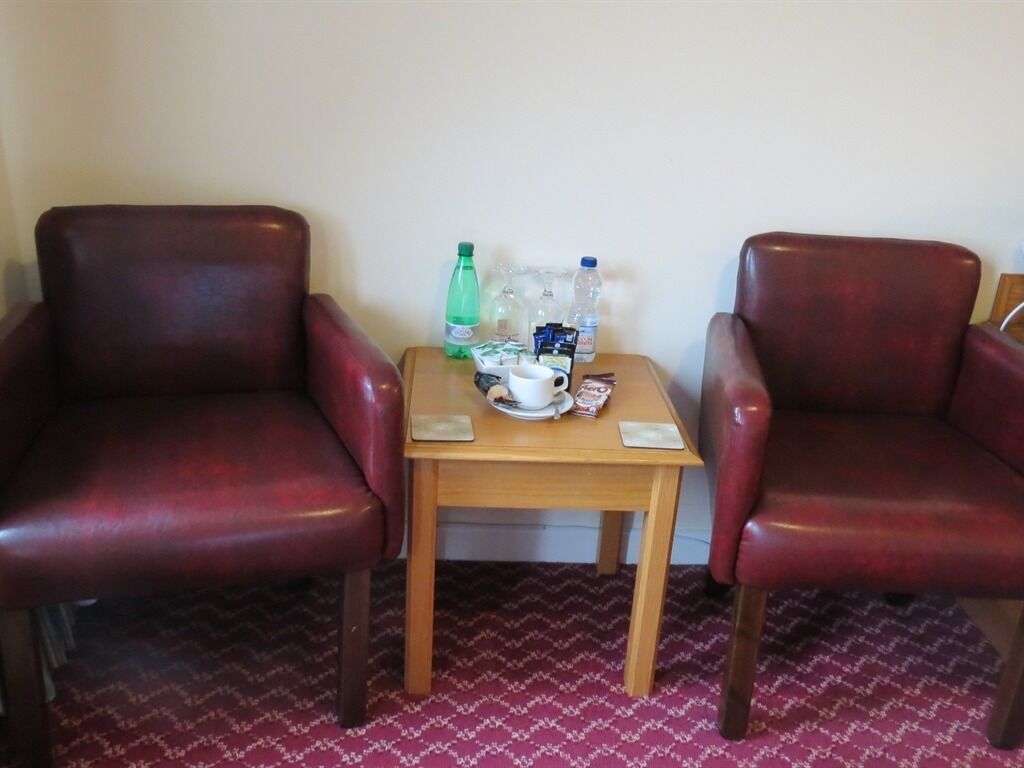 Two red leather chairs, a small wooden table with a white cup, a green bottle, and a clear plastic bottle.