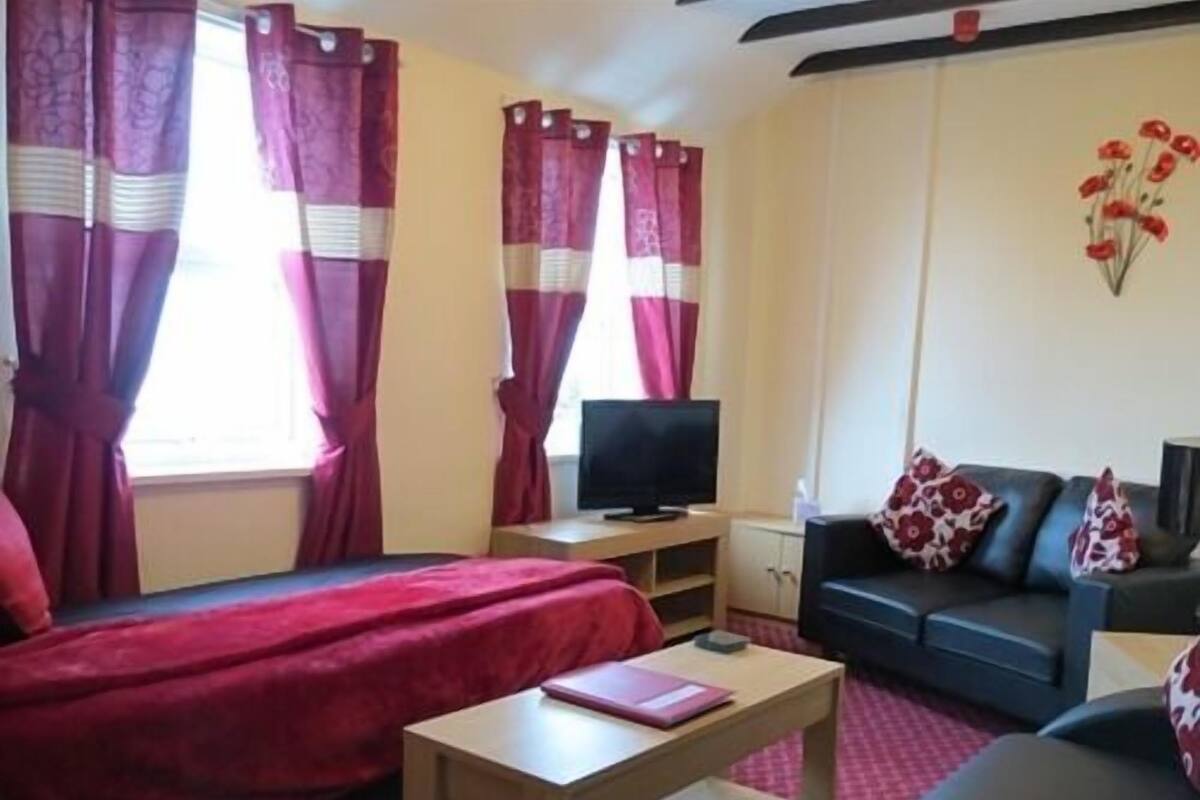 A living room with a sofa, a small table, a TV, and red curtains.