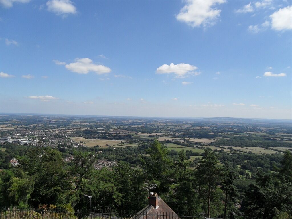 A panoramic view of a landscape with a distant town, surrounded by greenery and a clear sky.