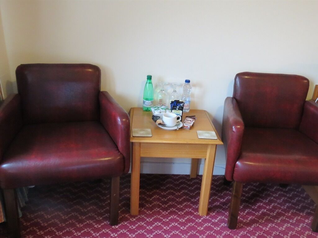 Una habitación con dos sillones de cuero y una pequeña mesa de madera con una taza, una botella y algunos aperitivos.