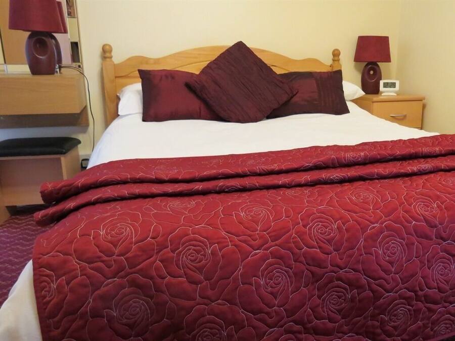 Un lit avec une tête de lit en bois, une couverture à motifs de roses rouges et un oreiller rouge.