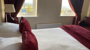 A hotel room with a bed, a lamp, a chair, and a view of the countryside through the window. - The Wyche Inn (Malvern)