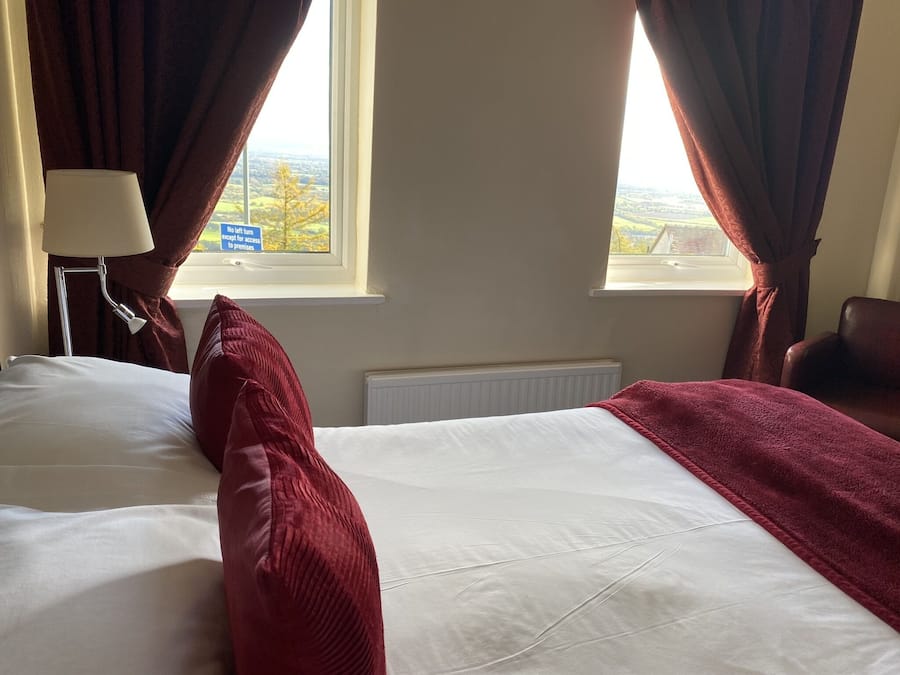 Habitación de hotel con cama, lámpara, silla y vista al campo por la ventana.