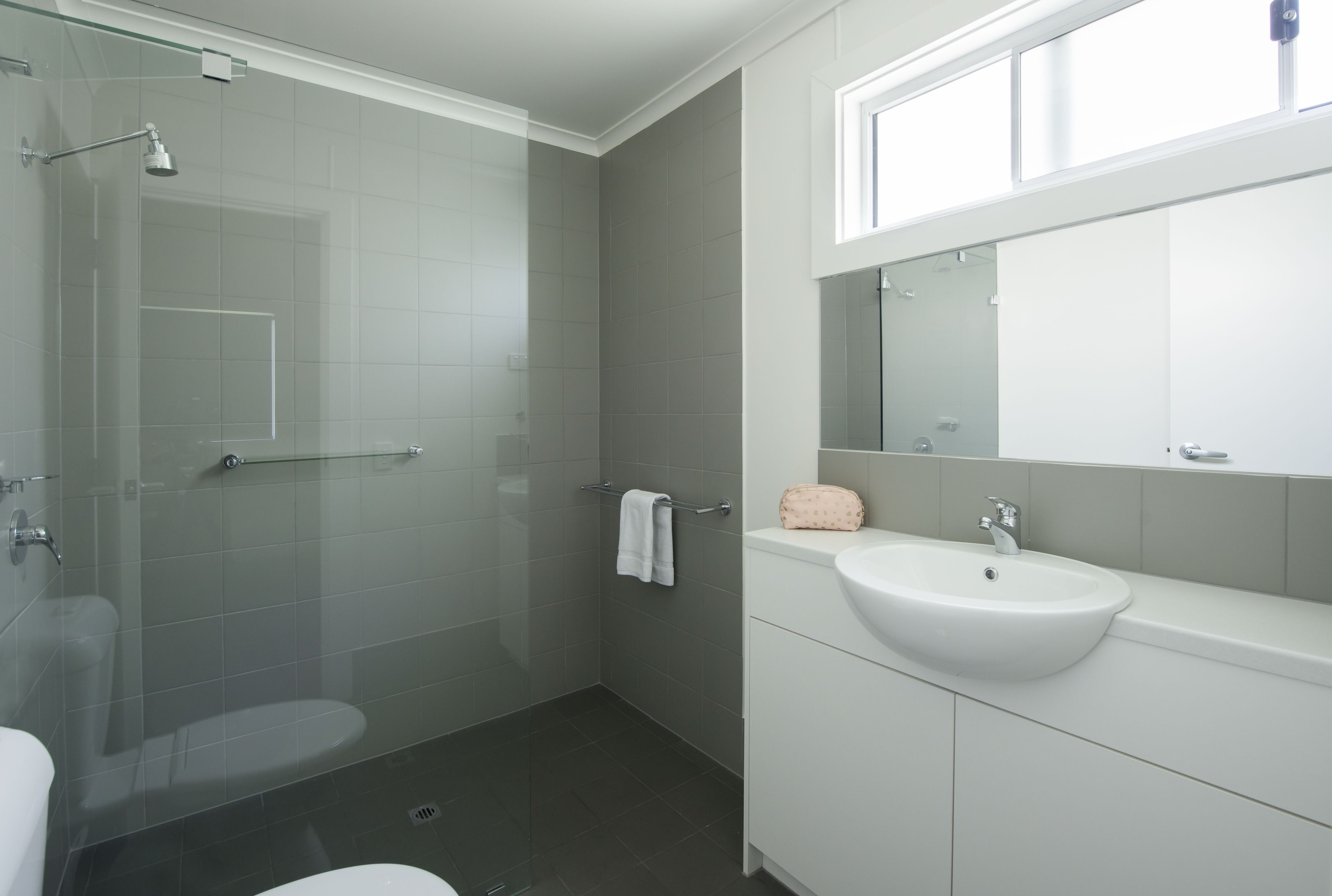 A modern bathroom with a glass-enclosed shower, a white sink, and a large mirror above the vanity.