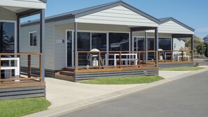 Une maison mobile moderne dotée d’un porche couvert, d’une petite terrasse et d’une enseigne de station-service bien visible.
