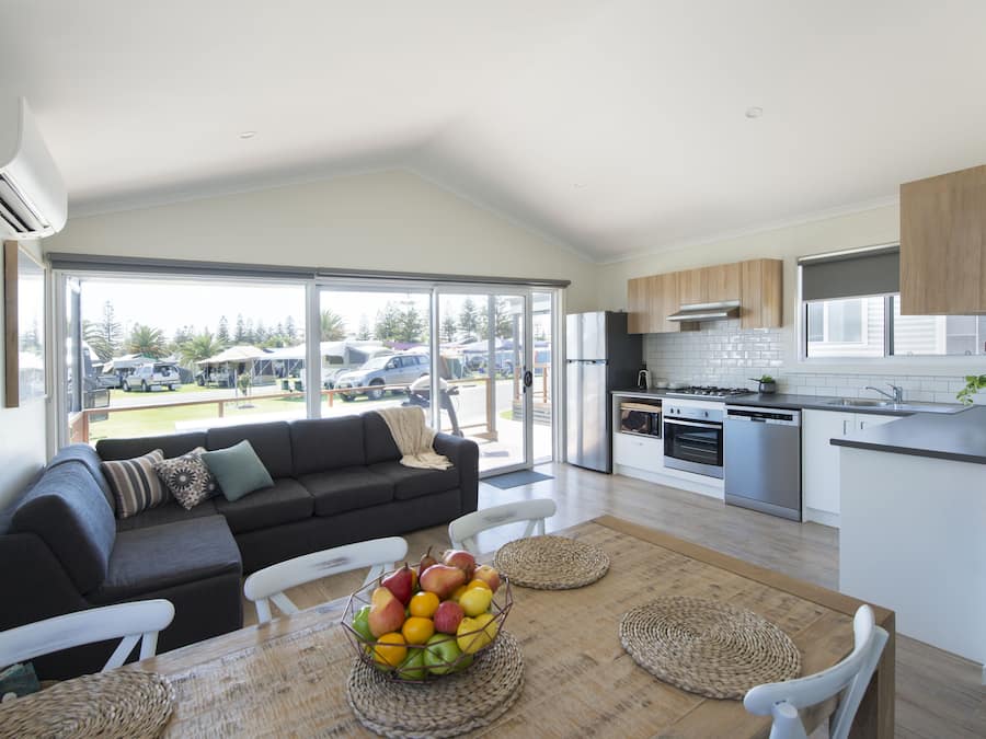 A modern kitchen with white cabinets, stainless steel appliances, and a large window overlooking a parking area.