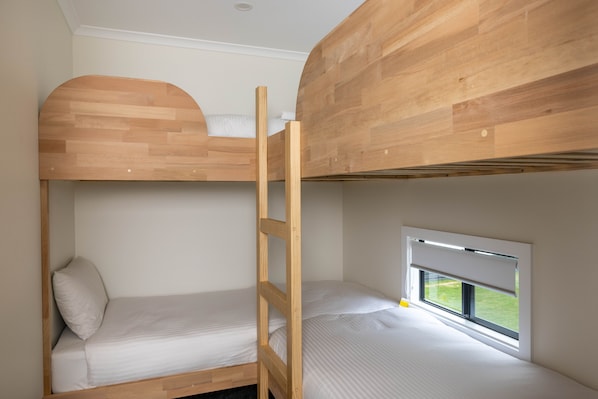 A bunk bed room with a wooden headboard, a window with a view, and a ladder.
