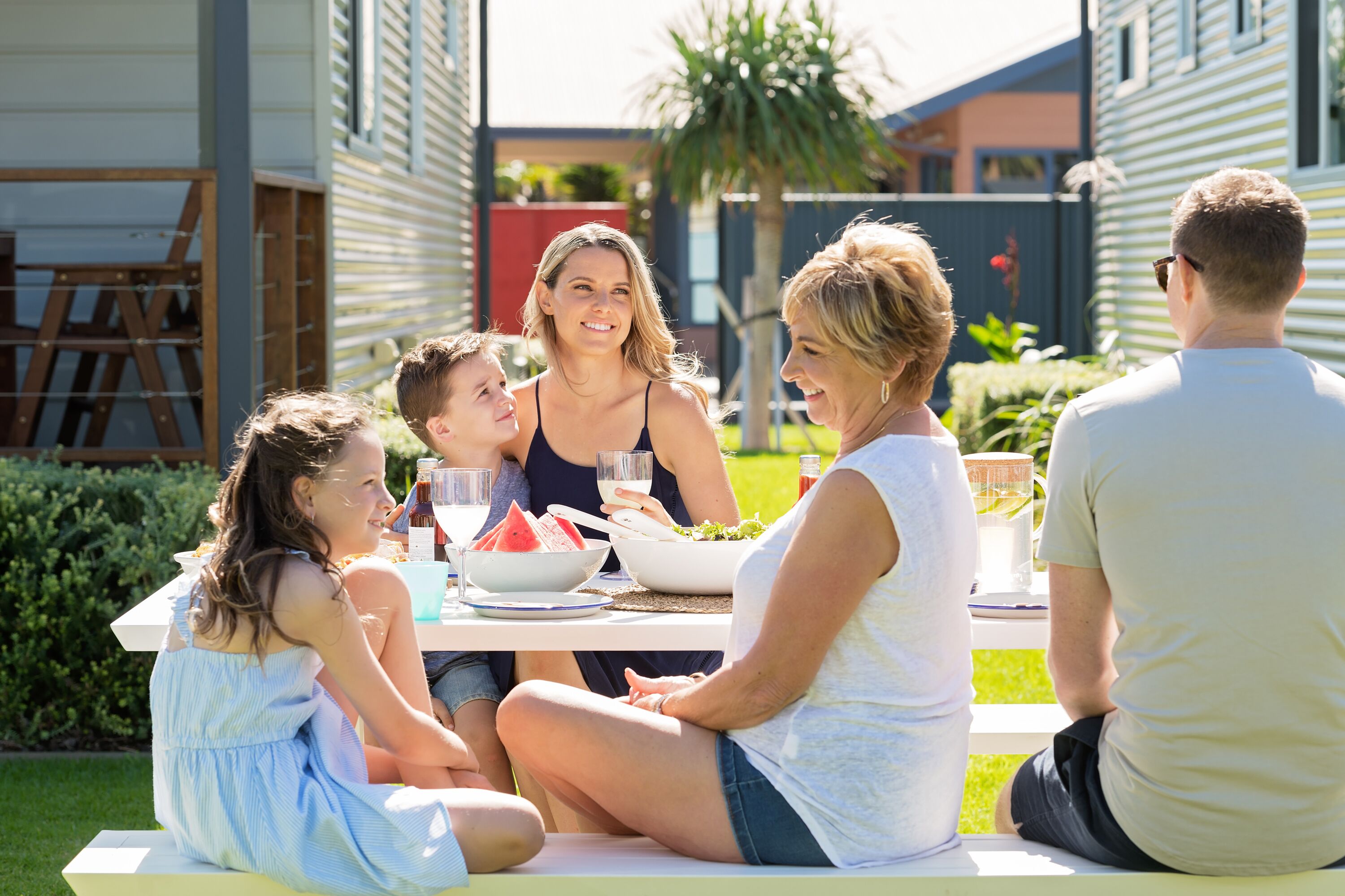 A family dining outdoors at a table with food and drinks.