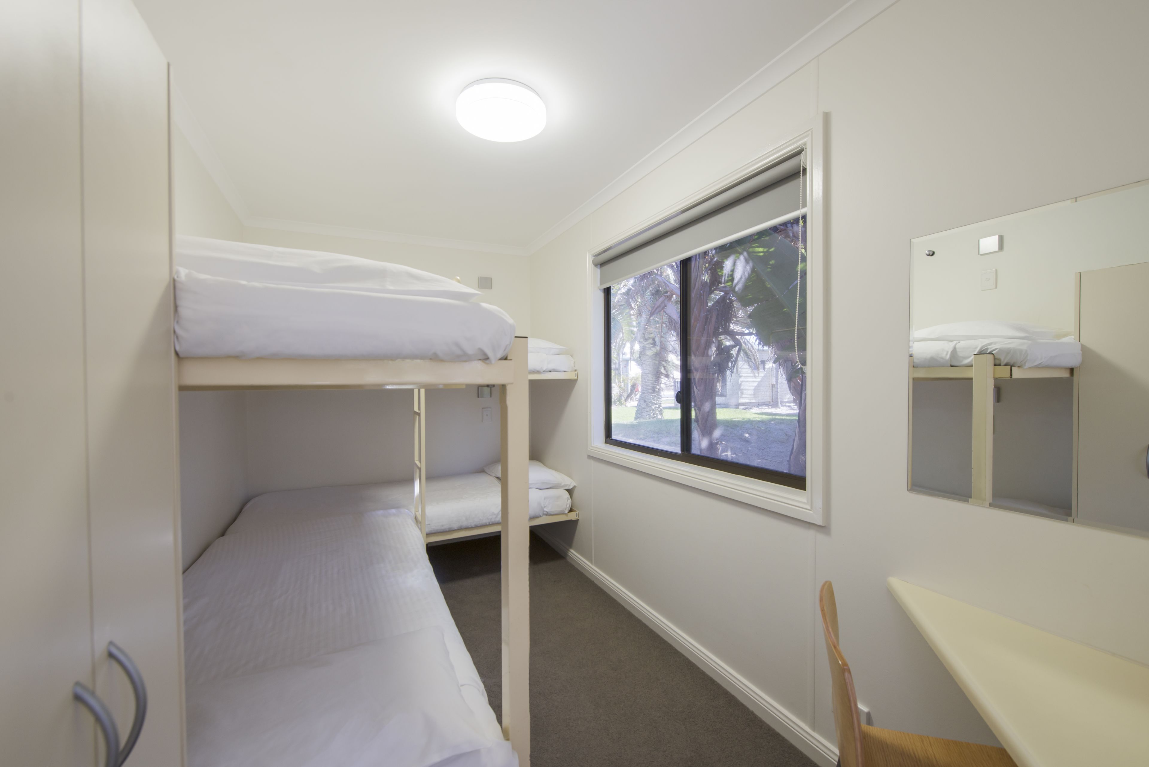A bunk room with two bunk beds, a window with a view of palm trees, and a small desk with a chair.