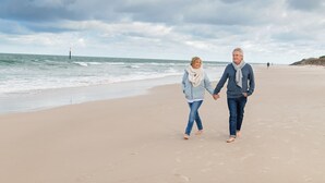 Un couple se promène sur une plage de sable, main dans la main, avec l’océan en arrière-plan.