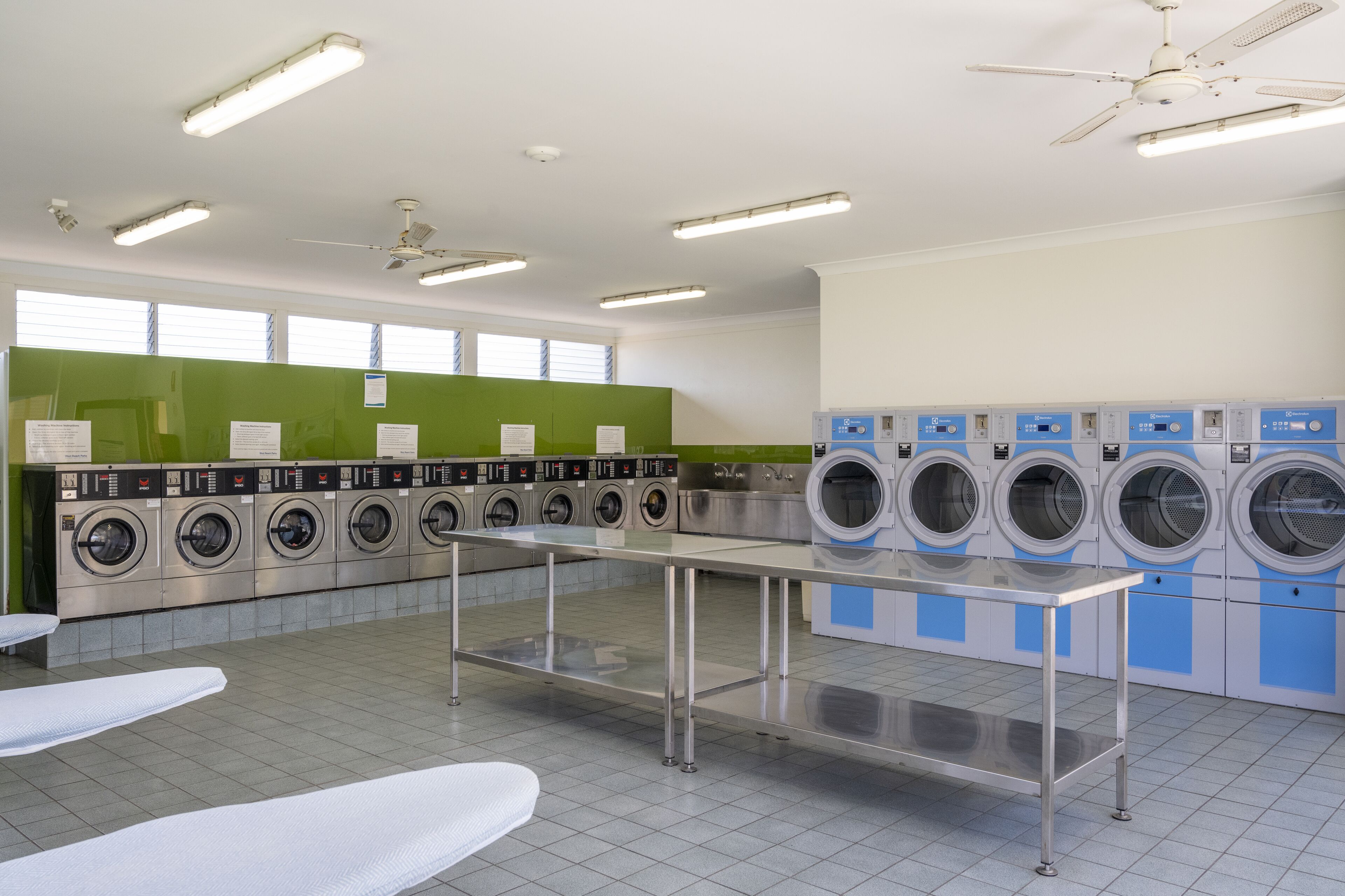 A laundry facility with multiple washing machines, a table, and ceiling fans.