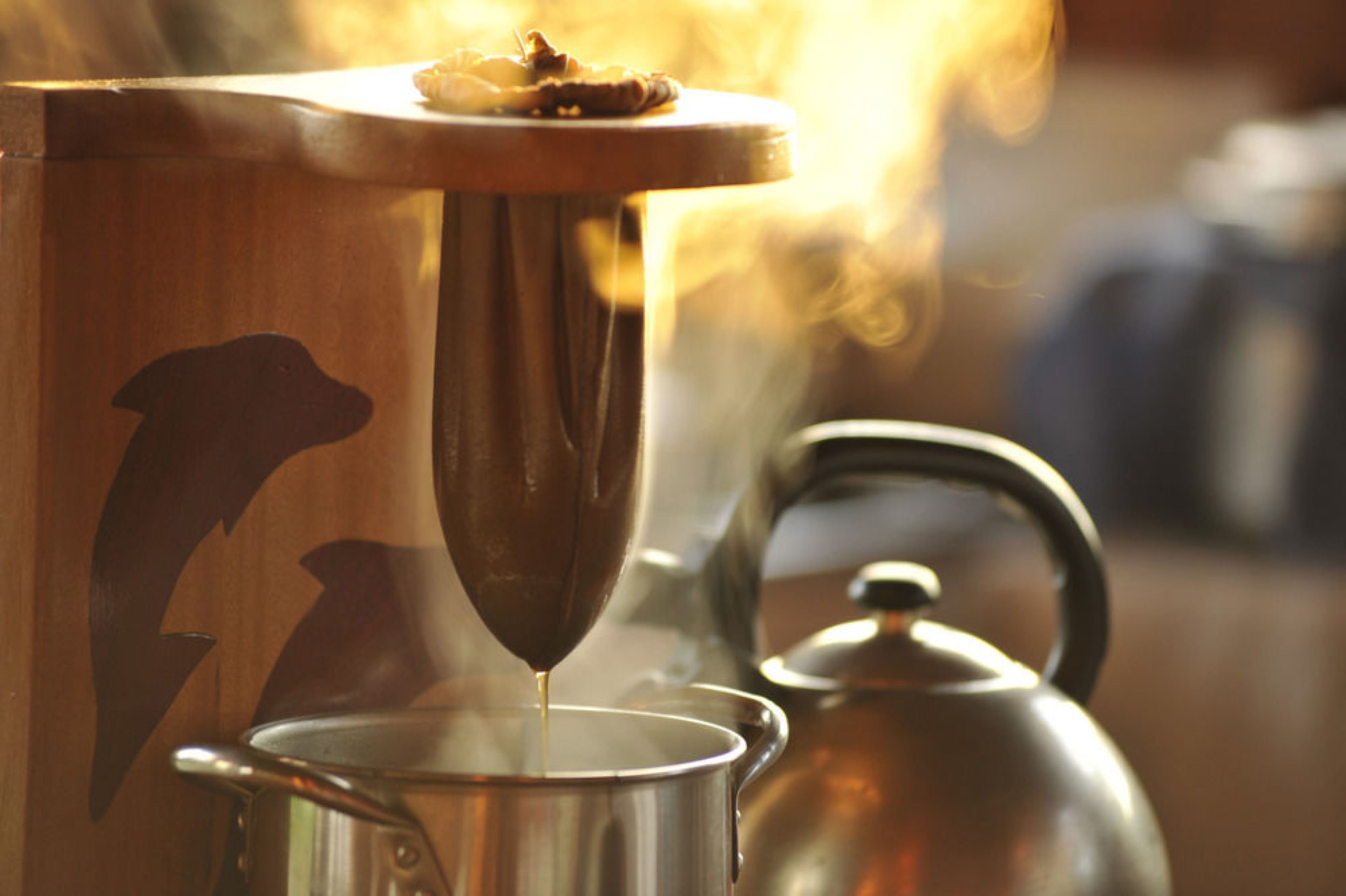 A wooden coffee maker with a dog silhouette, a kettle, and a pot on a stove.