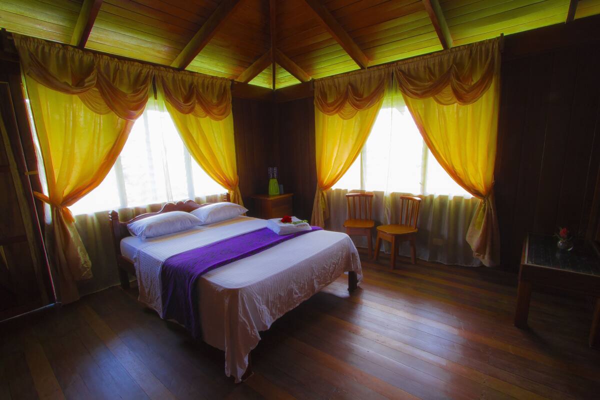 A room with a bed, a chair, a table, and curtains.