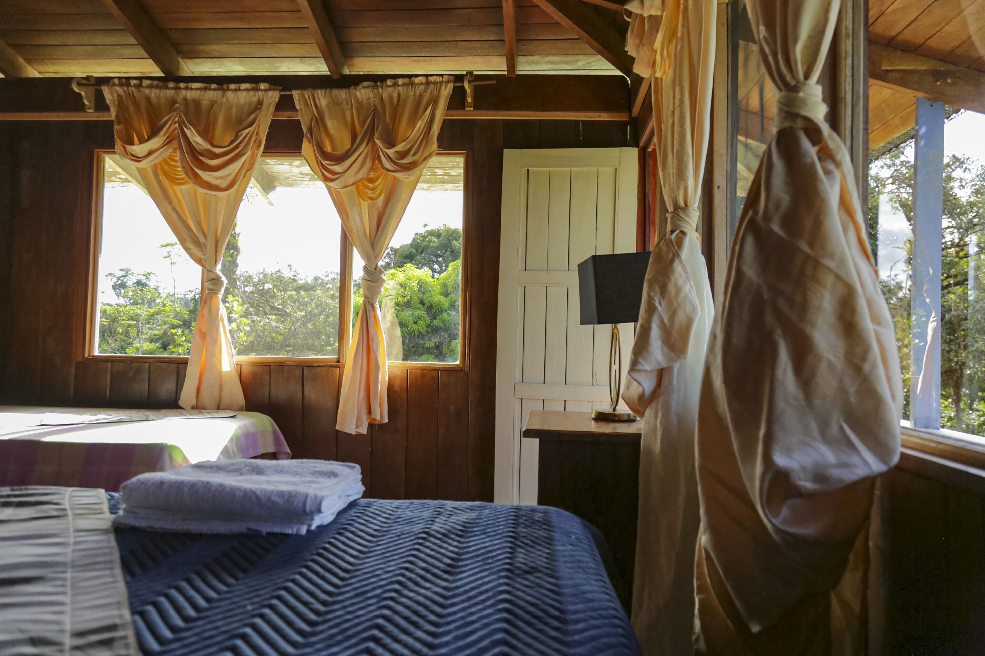 Une chambre avec deux lits, une fenêtre avec des rideaux, une porte et une table de chevet avec une lampe.