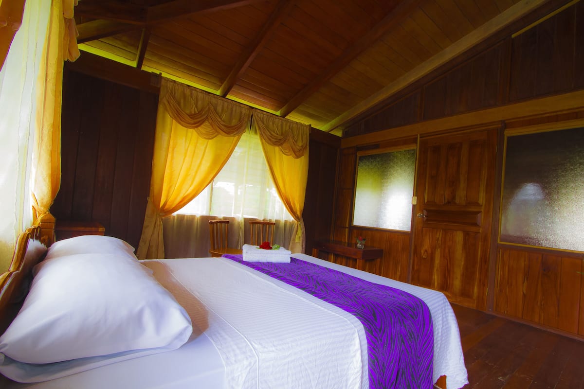 A wooden room with a bed, curtains, and a window.