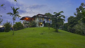 Une maison à deux étages dotée d’un balcon, entourée d’une végétation luxuriante et d’une pelouse bien entretenue.