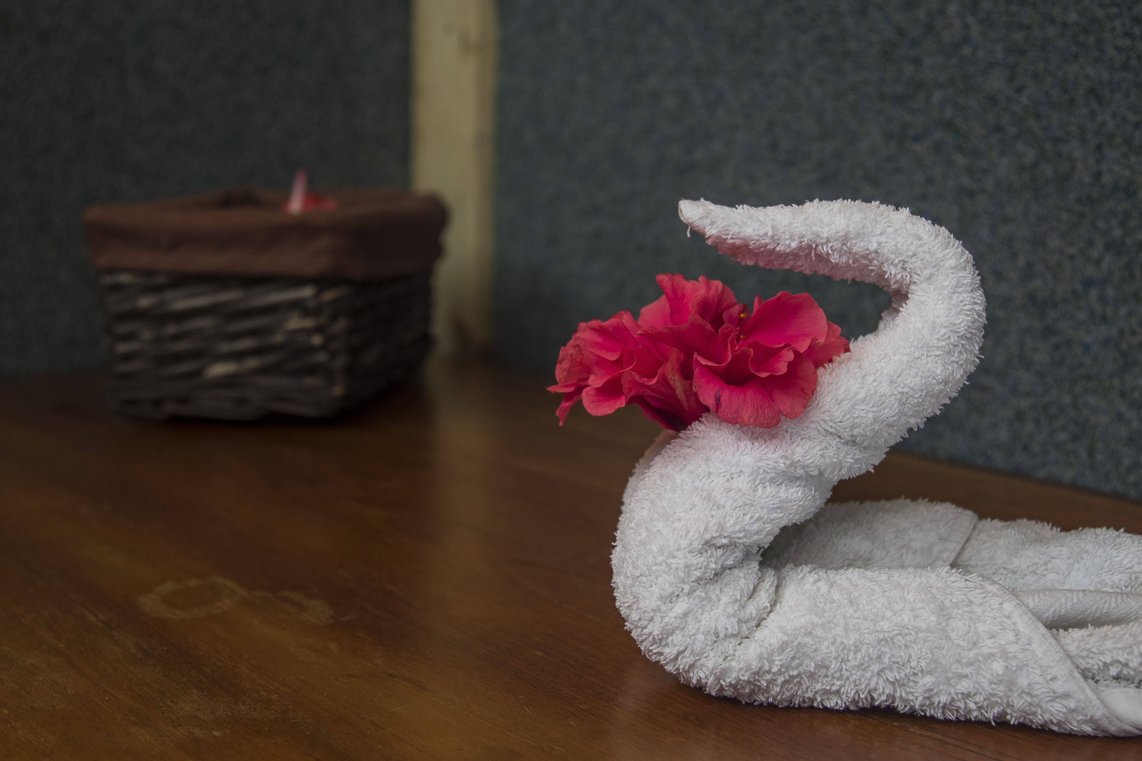 A swan-shaped towel with a pink flower on a wooden table.