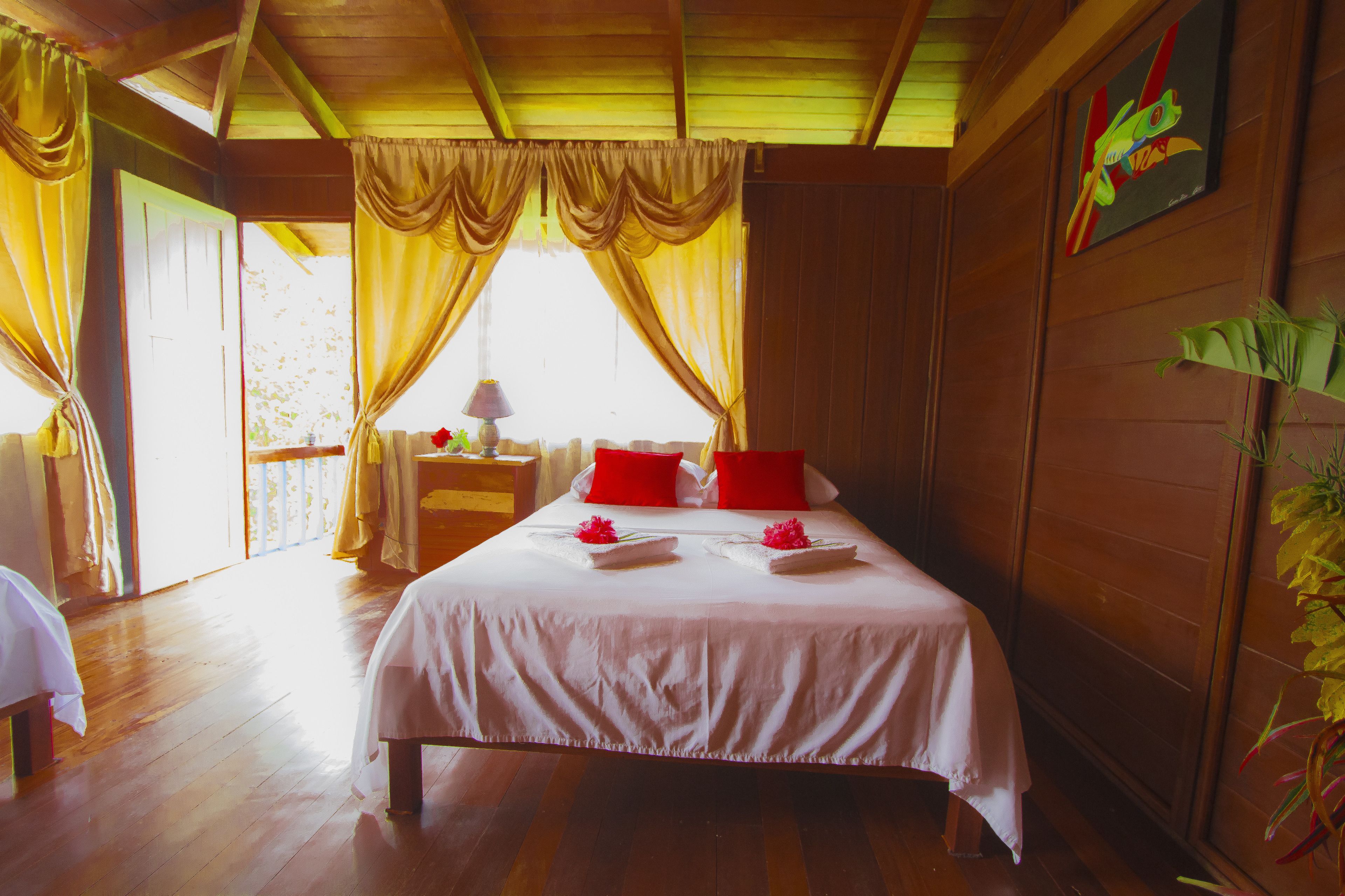 Una habitación con cama, cortinas, mesita de noche y una planta.