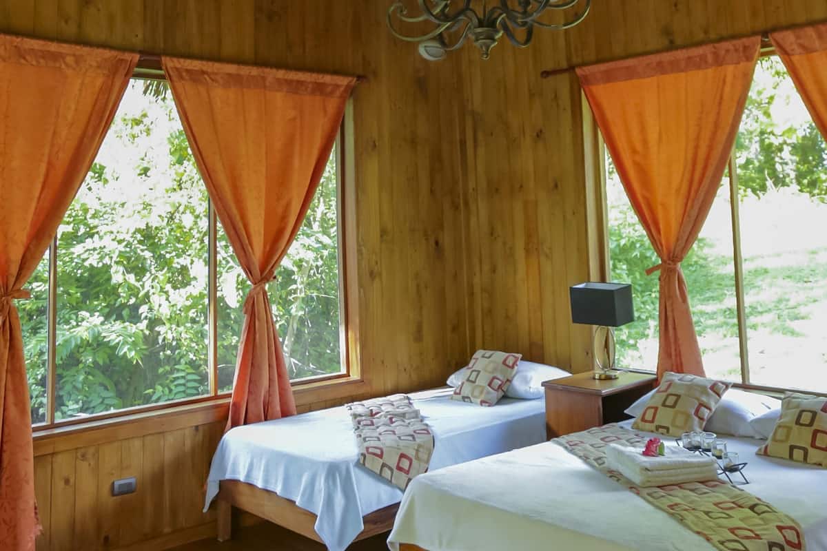 A wooden room with two beds, a chandelier, and orange curtains.