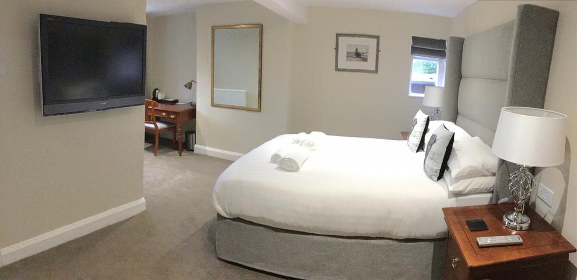 A hotel room with a large bed, a desk, a chair, a television, and a window.