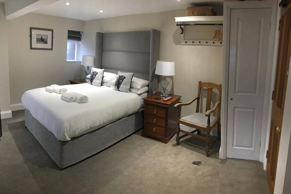 Quarto com cama grande, mesa de cabeceira com abajur, cadeira e guarda-roupa.