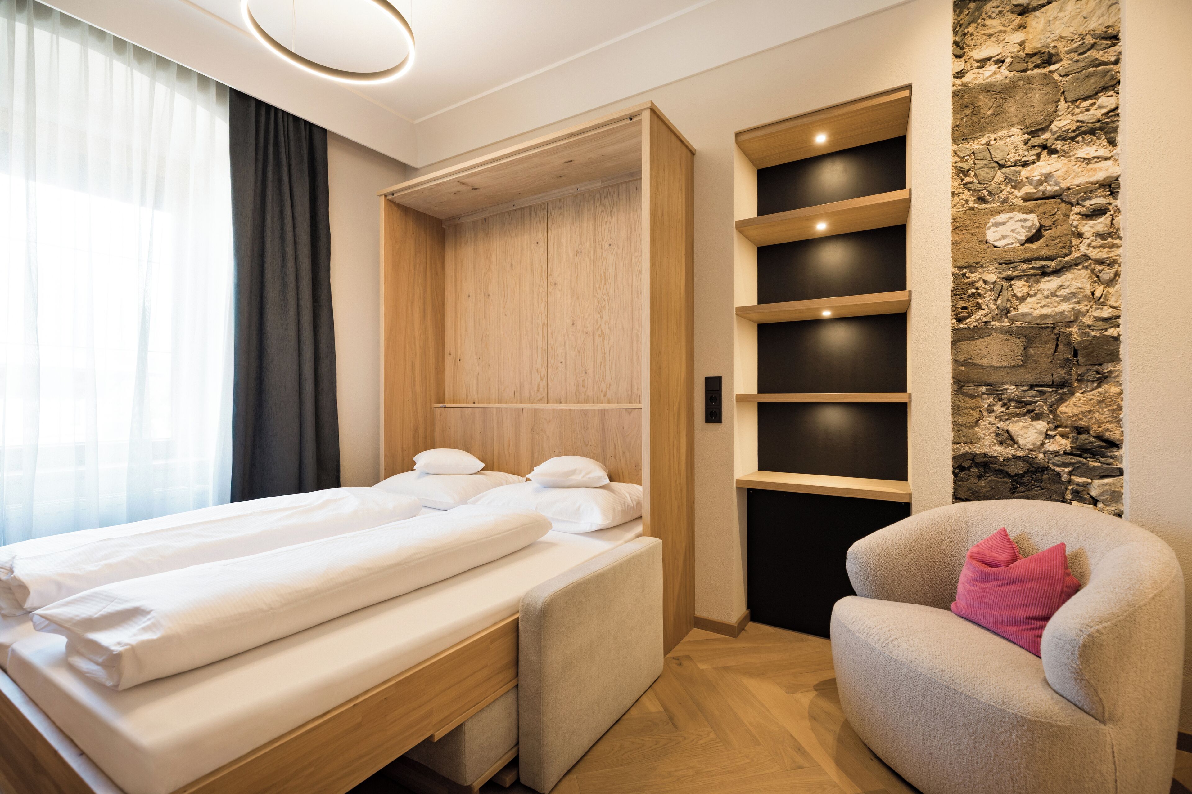 Un dormitorio con cama, una silla, un armario y una pared de piedra.