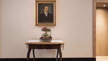 Un retrato enmarco en una pared, una pequeña mesa con un arreglo floral y suelo de madera.
