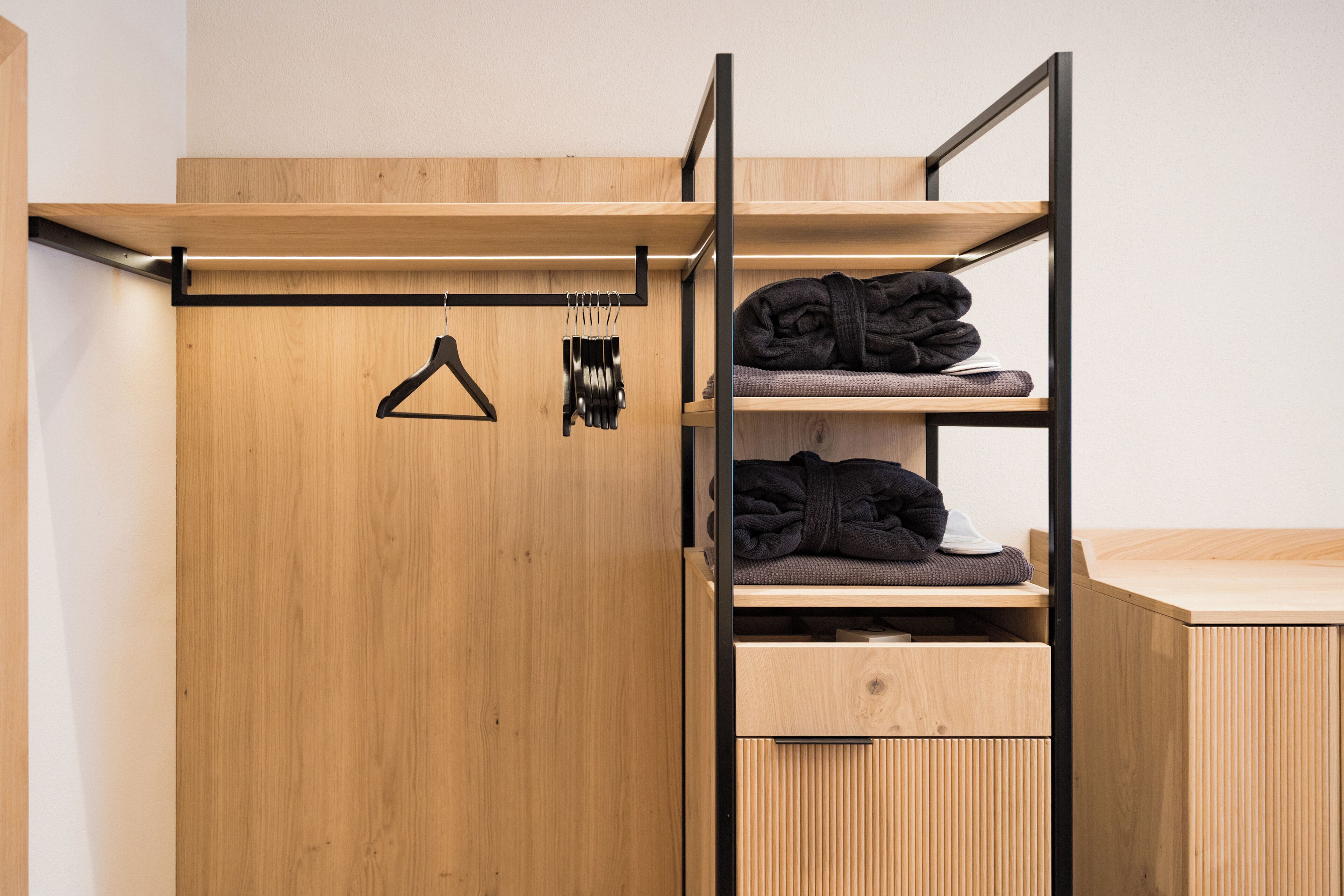 A wooden wardrobe with a hanging rack and shelves for folded clothes.