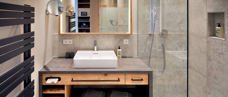 A modern bathroom with a large mirror, a sink, a shower, and a towel rack.