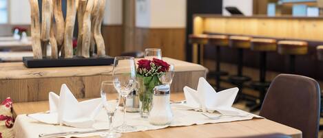 A dining table set with white napkins, a salt and pepper shaker, a vase with red roses, and a modern lamp.