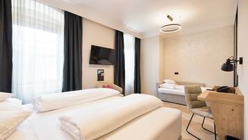 A hotel room with two beds, a desk, a chair, a TV, and a large window with curtains.