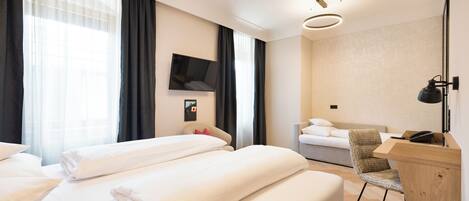 Habitación de hotel con dos camas, un escritorio, una silla, un televisor y un ventanal con cortinas.