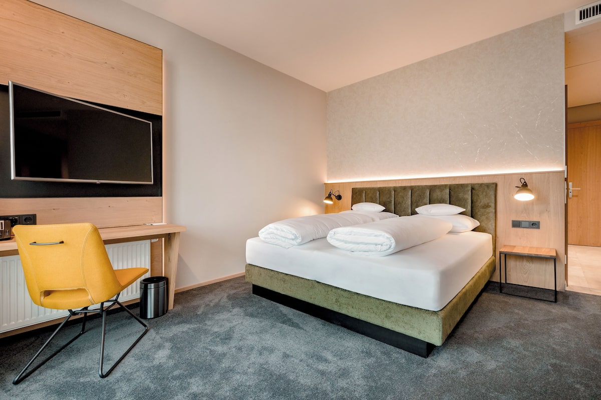 Ein modernes Hotelzimmer mit Bett, Schreibtisch, Stuhl und Fernseher.