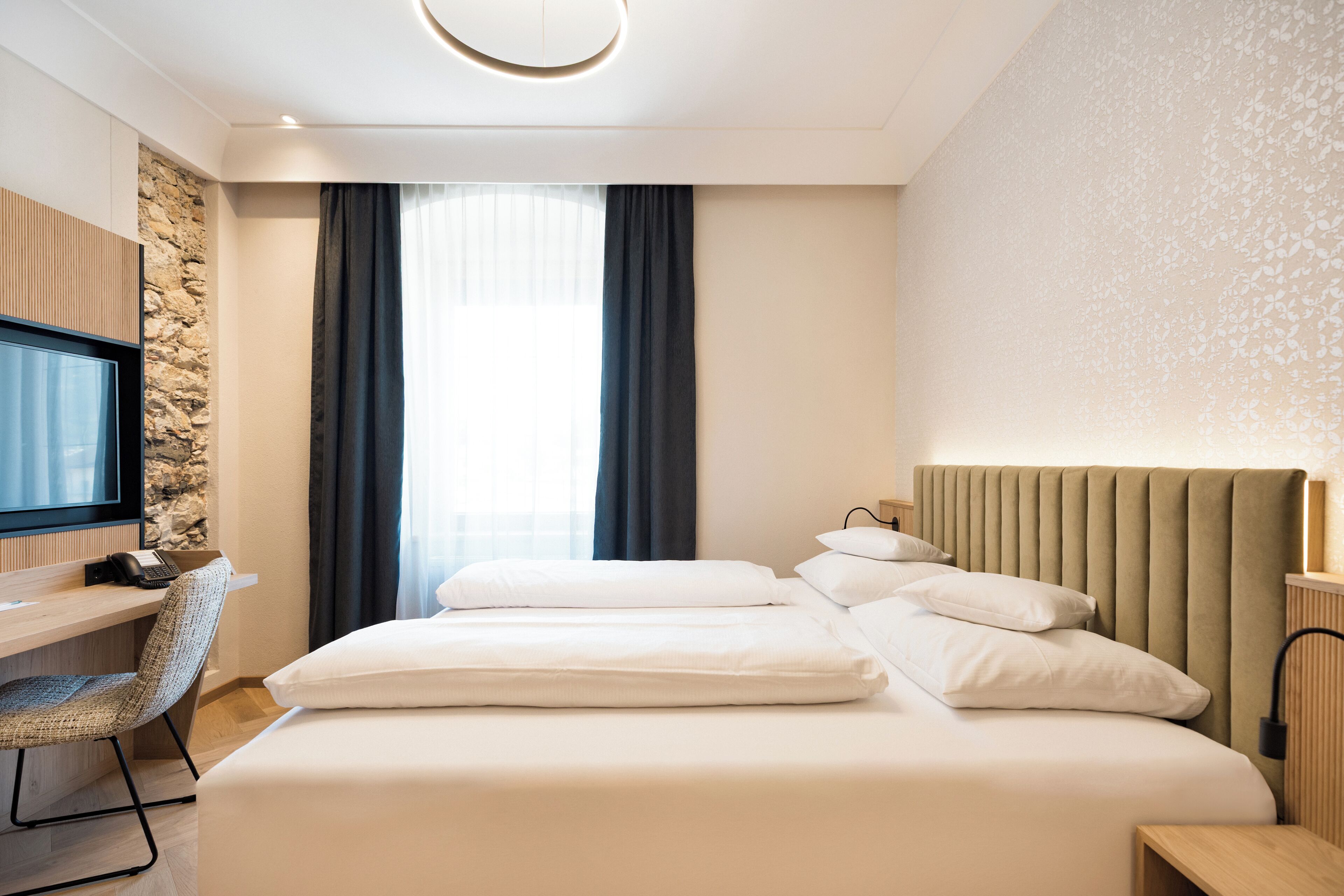 Een hotelkamer met een bed, bureau, stoel, televisie en raam met gordijnen.